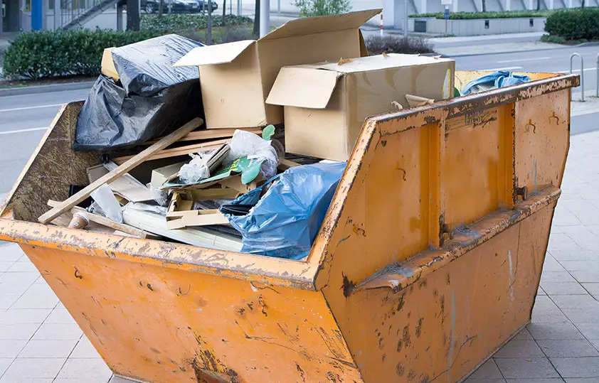 Ein Container voller Kartons und Gerümpel steht vor einem Gebäude